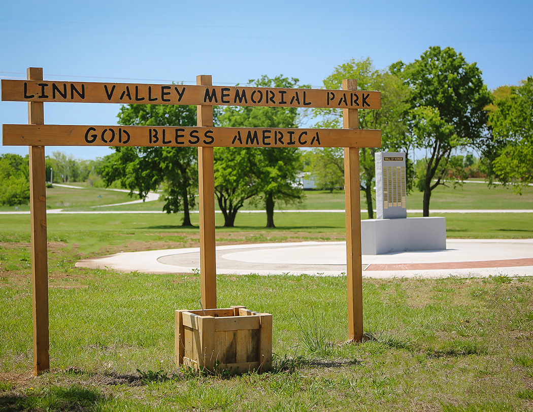 The "Linn Valley Memorial Park — God Bless America" wooden entrance sign with the Wall of Honor in the background.